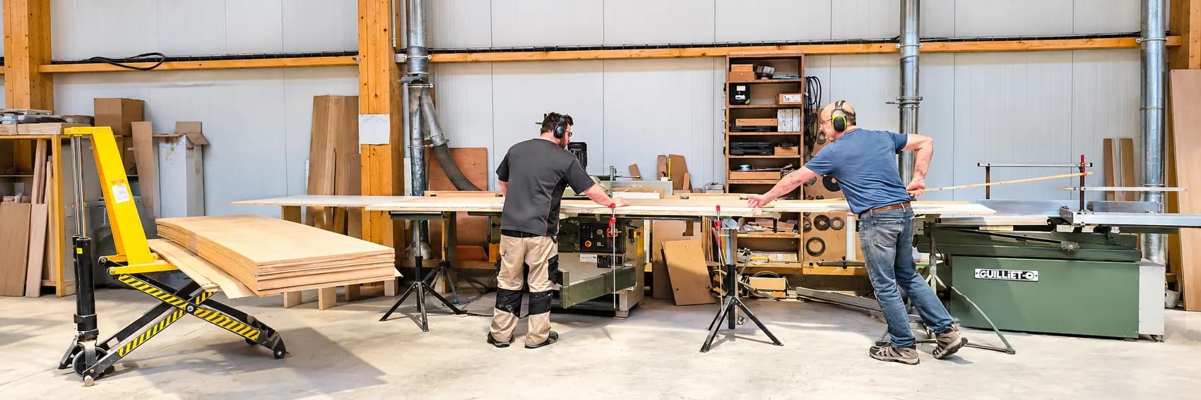 L’atelier d’Auzebosc : deux ébénistes Auboi engagent un panneau de hêtre dans la scie à format, panneaux et table élévatrice sur la gauche