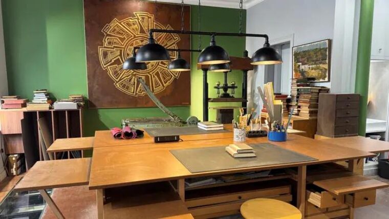 Atelier de Bourgogne Reliure : table de travail Auboi sous trois suspensions, presse à dorer et bibliothèque le long du mur vert