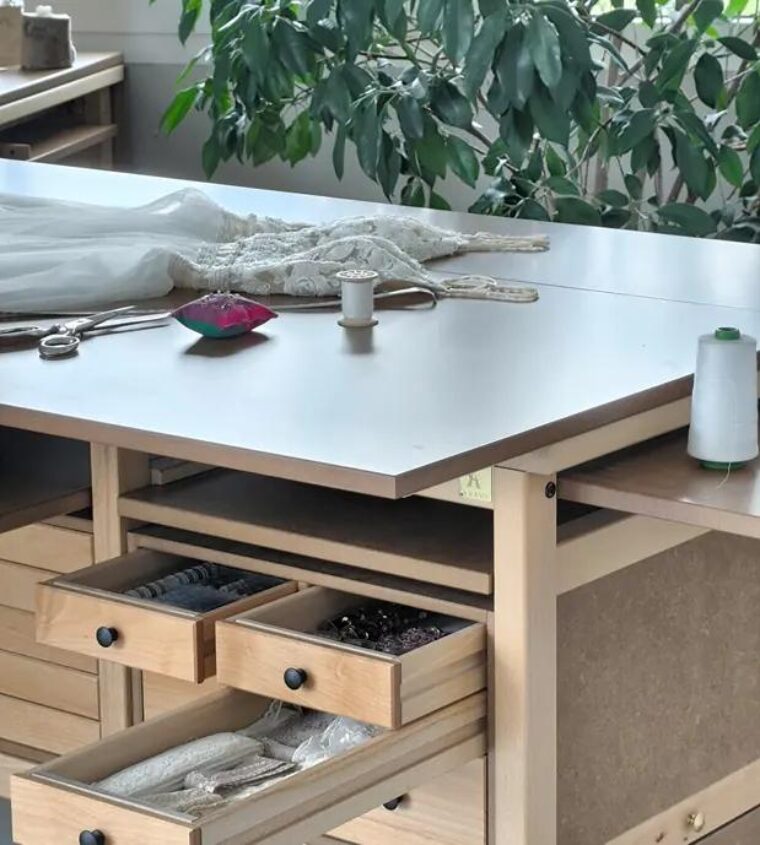 Confection d’une robe de mariée sur une Table Atelier Auboi : la dentelle étalée sur le plateau, tiroirs de mercerie ouverts au-dessous