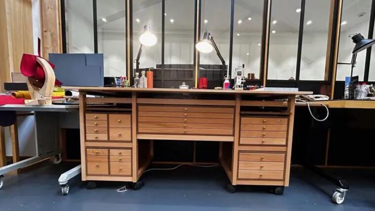 Bureau d’atelier Auboi à double caisson de tiroirs devant une verrière, deux lampes articulées et le matériel de découpe posés sur le plateau