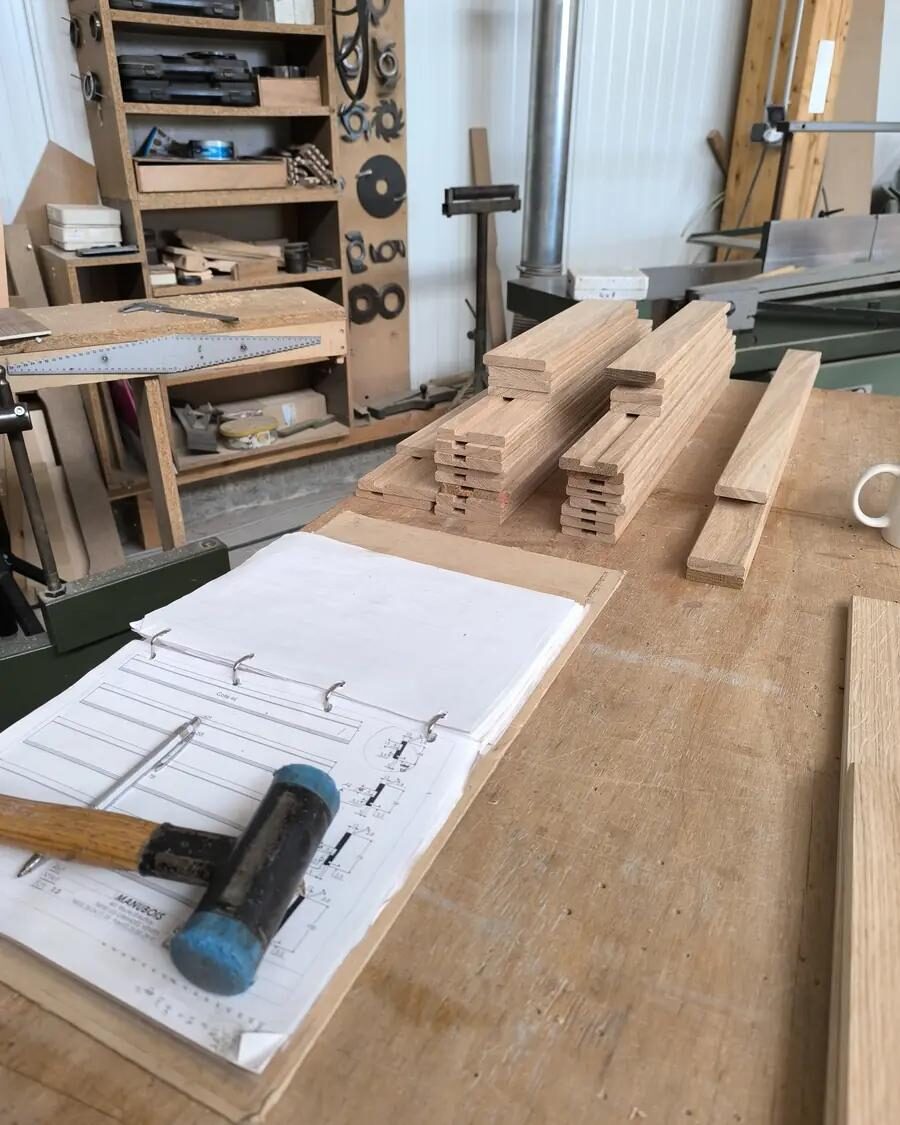 L’établi de l’atelier d’Auzebosc : carnet de croquis ouvert, maillet, pièces de hêtre en attente d’assemblage
